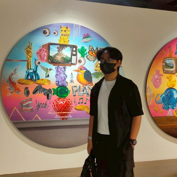 Muhammad Aristya Prayitno standing in front of a colorful round painting at an art exhibition